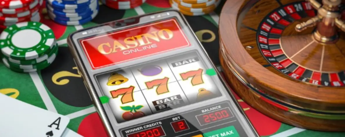 Fichas de casino, roleta e cartas do baralho com foco no slot no ecrã do telemóvel.